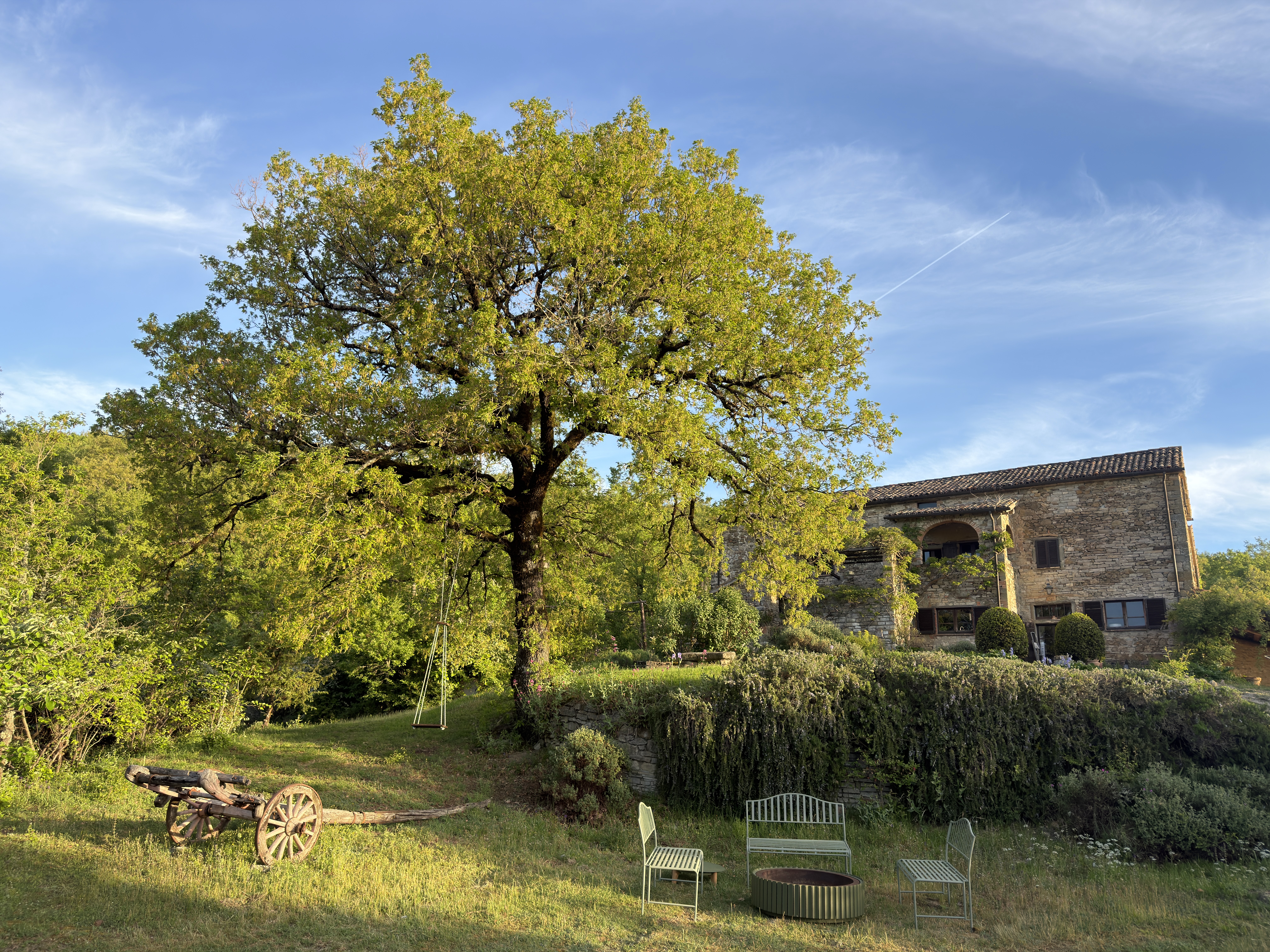 Villa exterior with oak tree, old cart, swing and fire pit seating