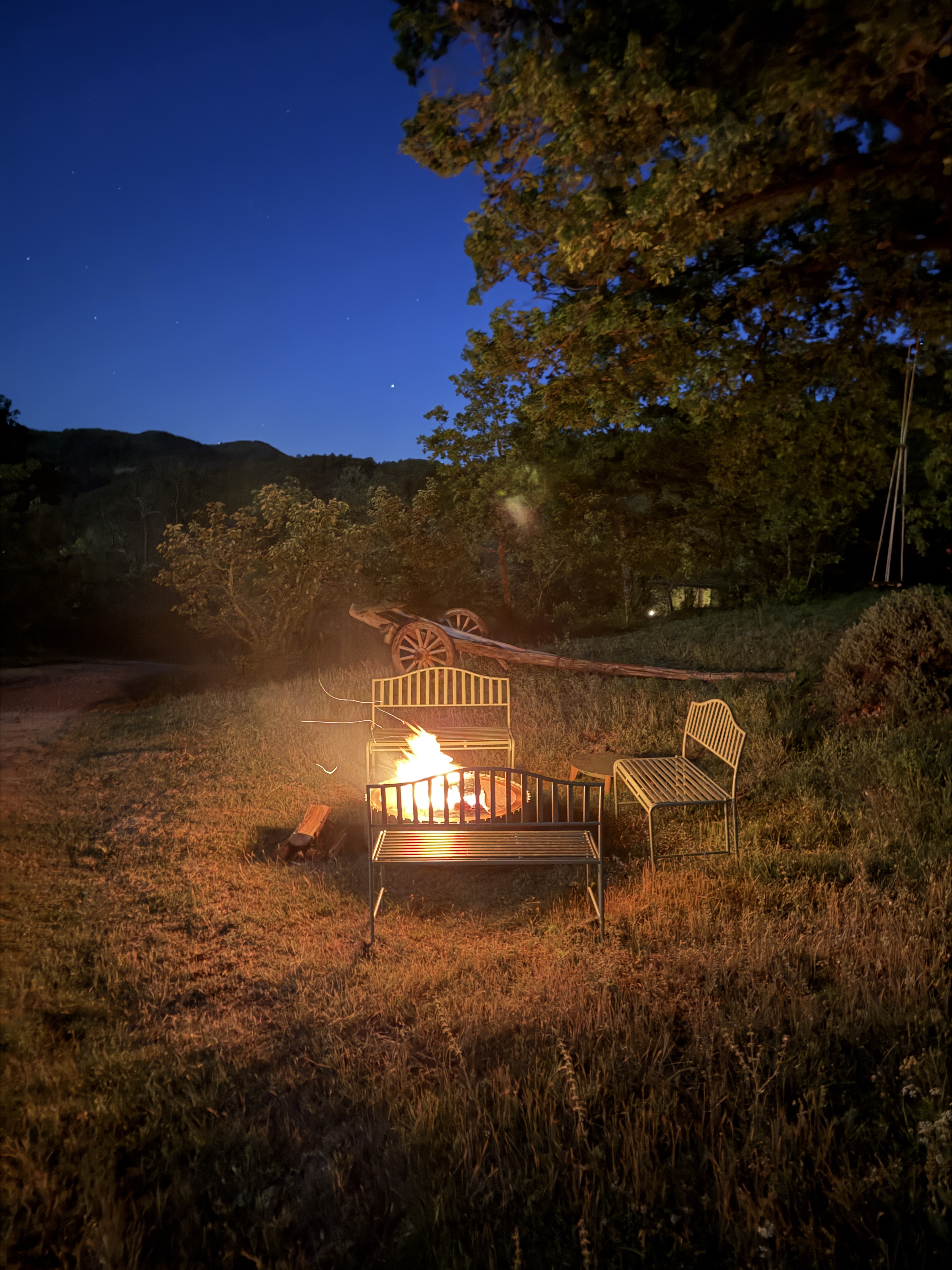 Fire pit burning at night under starlit sky with metal benches